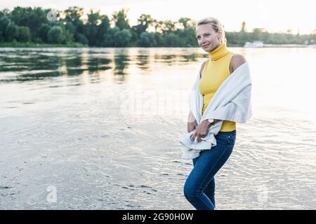 Frau in Decke gehüllt und schaute weg, während sie am Flussufer spazieren ging Stockfoto