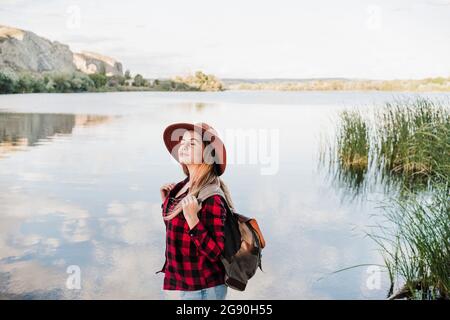 Junge, schöne Frau mit Hut und geschlossenen Augen am Seeufer Stockfoto