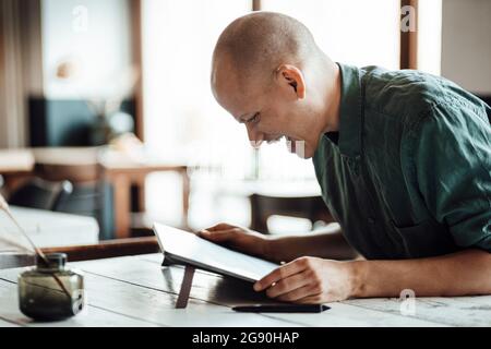 Glücklicher kahler Geschäftsmann, der im Café auf ein digitales Tablet schaut Stockfoto