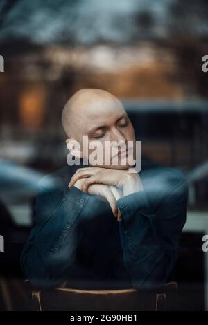 Ein Geschäftsmann, der mit der Hand am Kinn im Cafe durch das Fenster gesehen, zu einem Nickerchen aufmachte Stockfoto