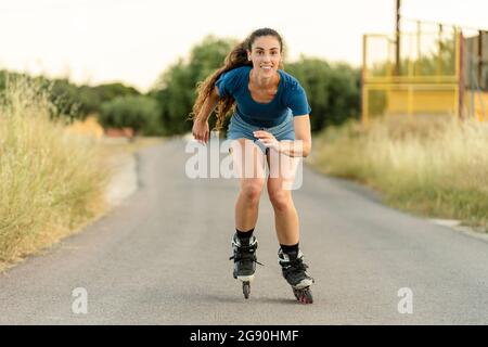 Lächelnde junge Frau Rollschuh auf der Straße Stockfoto