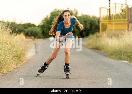 Junge Frau mit langen Haaren genießt Inline-Skating auf der Straße Stockfoto