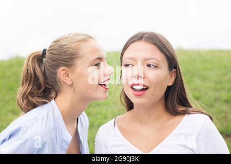 Junge Frau flüstert zu einer Freundin in der Natur Stockfoto