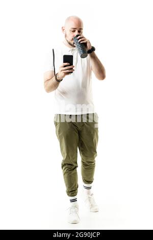 Beschäftigt junge nerdy Hipster-Stil Mann trinken Kaffee zu Fuß und mit dem Smartphone. Porträt in voller Länge isoliert auf weißem Hintergrund Stockfoto