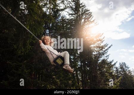 Lächelndes Mädchen schwingt auf Seilschaukel im Wald Stockfoto