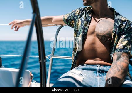 Hipster-Mann mit unknöpfbarem Hemd sitzt an sonnigen Tagen auf der Yacht Stockfoto