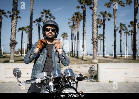 Junger Mann mit Helm, während er an sonnigen Tagen auf dem Motorrad sitzt Stockfoto