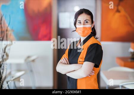 Kellnerin trägt eine schützende Gesichtsmaske und steht während einer Pandemie in der Cafeteria Stockfoto