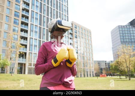 Ältere Frau mit Boxhandschuhen und Virtual-Reality-Headset im Park Stockfoto