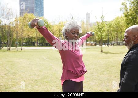 Mann, der eine ältere Frau beim Training mit Hanteln im Park ansieht Stockfoto