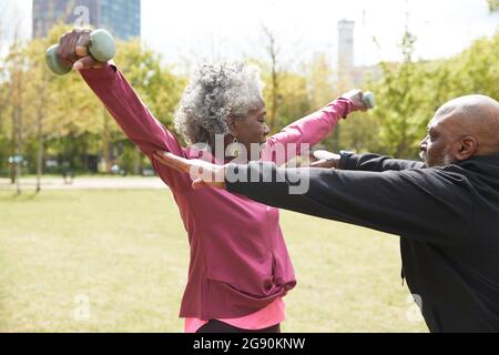 Mann, der einer älteren Frau beim Training mit Kurzhanteln im Park hilft Stockfoto