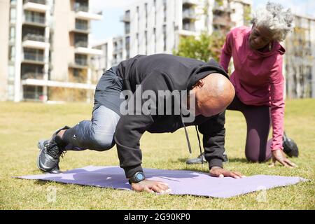 Ältere Frau, die dem Mann bei der Ausübung im öffentlichen Park hilft Stockfoto