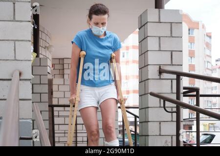 Eine Frau mit gebrochenem Bein geht mit orthopädischen Krücken eine Rampe hinunter. Stockfoto