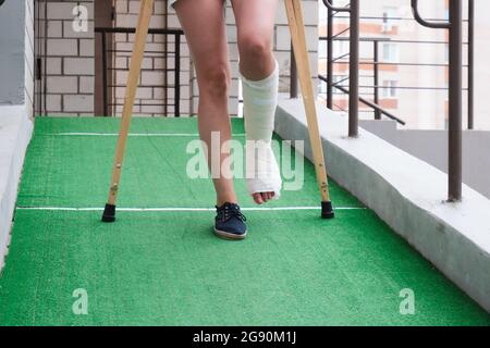 Eine Frau mit gebrochenem Bein geht mit orthopädischen Krücken eine Rampe hinunter. Stockfoto