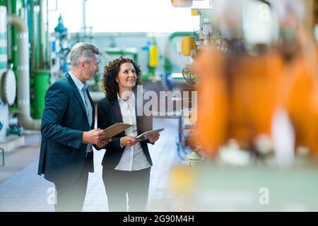 Männliche und weibliche Inspektoren überprüfen Maschine, während sie in der Industrie stehen Stockfoto