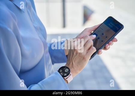 Geschäftsfrau mit smarter Armbanduhr über Mobiltelefon Stockfoto