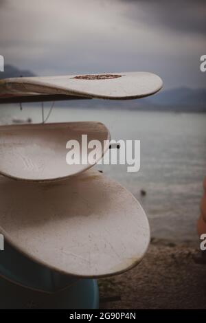 Am Ufer eines Sees werden verschiedene Surfbretter übereinander gestapelt Stockfoto