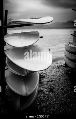 Am Ufer eines Sees werden verschiedene Surfbretter übereinander gestapelt Stockfoto