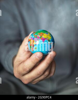 Ein kurzer Mann hält einen kleinen Globus in der Hand auf einem grauen Hintergrund. Stockfoto