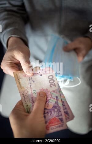 Spekulation auf medizinische Masken. Menschen illegal verkaufen Masken sehr teuer, weil sie in knapper Versorgung sind. Hände passieren Masken für Geld, ukrainische hryvn Stockfoto