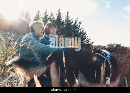 Ältere Frau und ihre Tochter lächeln und haben Spaß in der Natur mit ihrem Hund Stockfoto