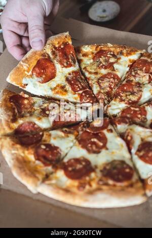 Ein kurzer Mann nimmt ein Stück Pizza mit der Hand. Selektiver Fokus, Unschärfe, Nahaufnahme Stockfoto