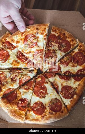 Ein kurzer Mann nimmt ein Stück Pizza mit der Hand. Selektiver Fokus, Unschärfe, Nahaufnahme Stockfoto