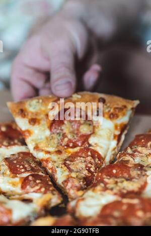 Ein kurzer Mann nimmt ein Stück Pizza mit der Hand. Selektiver Fokus, Unschärfe, Nahaufnahme Stockfoto