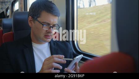 Junger Mann, der Zelle benutzt, um im Zug online zu surfen Stockfoto