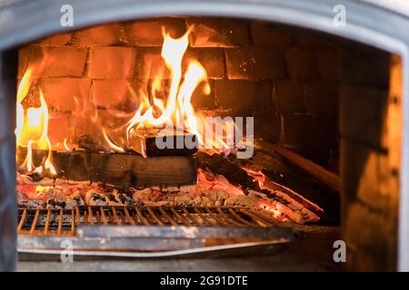 Ein traditioneller Ofen mit brennendem Feuer zum Kochen. Feuerholz und Kohlen brennen im Inneren. Innenansicht. Stockfoto