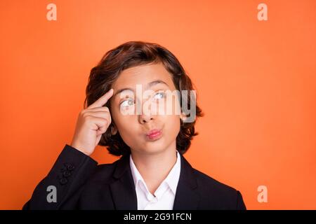 Foto von jungen gesinnten nachdenklichen kleinen Jungen halten Finger Tempel suchen leeren Raum isoliert auf orangefarbenen Hintergrund Stockfoto