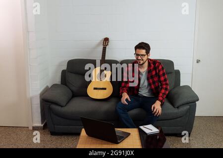 Der Lateinmann sitzt mit seiner Gitarre vor seinem Notizbuch. Stockfoto