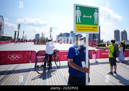 Tokio, Japan. Juli 2021. Besucher schauen auf die olympische Flamme. Ein Mitarbeiter hält ein Schild mit einem Symbol und den Worten „Keep physical distance“, um sich und andere vor dem Coronavirus zu schützen. Die Olympischen Spiele 2020 in Tokio finden vom 23. Juli 2021 bis zum 8. August 2021 statt. Quelle: Michael Kappeler/dpa/Alamy Live News Stockfoto