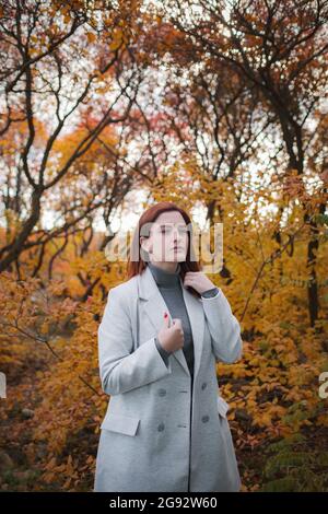 Eine niedliche rothaarige Frau in guter Laune posiert an einem Herbsttag und genießt das schöne Wetter. Das Konzept und die Idee, Herbst und Herbst Getaway zu genießen Stockfoto