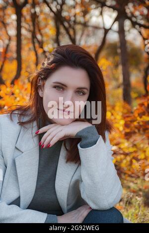 Eine niedliche rothaarige Frau in guter Laune posiert an einem Herbsttag und genießt das schöne Wetter. Das Konzept und die Idee, Herbst und Herbst Getaway zu genießen Stockfoto