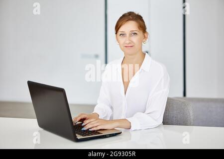 Selbstbewusste junge Frau sitzt im Büro und arbeitet mit einem Laptop. Stockfoto