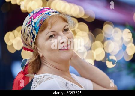 Ältere fröhliche Dame im Kopftuch posiert draußen für das Porträt. Stockfoto