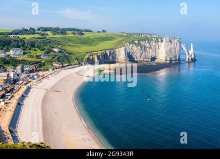 Blick auf die Küste und den Kiesstrand von Etretat in der Normandie mit der Nadel und dem Bogen der Aval-Klippe in der Ferne an einem sonnigen Tag. Stockfoto