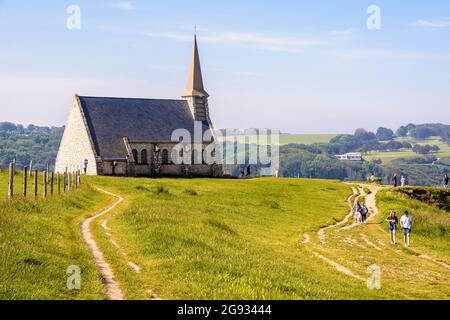 Touristen, die an einem sonnigen Frühlingsmorgen auf der Klippe des Amont in Etretat, Normandie, an der Kapelle Notre-Dame de la Garde vorbeischlendern. Stockfoto