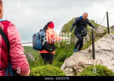 Ein Guide, der einer Wanderin beim Überqueren des Kozya Stena Peak oder der Chamoiswand auf dem E3-Pfad im bulgarischen Zentralbalkan ein Metallseil verwendet Stockfoto