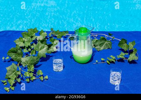Ein blaues Strandtuch am Pool wird als Tischdecke mit zwei Gläsern mit Eiswürfeln und Mineralwasser und einem Krug Grapefruitsaft verwendet Stockfoto