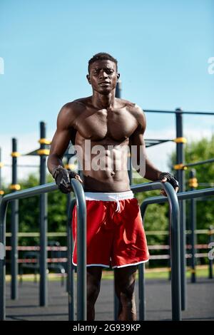 Junge Athletin afroamericatsen, die auf den unebenen Riegel trainieren, ein Athlet in hervorragender körperlicher Verfassung, der auf der Straße auf dem Spielplatz Übungen macht. Stockfoto