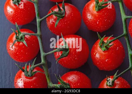 Frische reife rote Tomaten auf Ast mit Wassertropfen auf Holzbrett Stockfoto