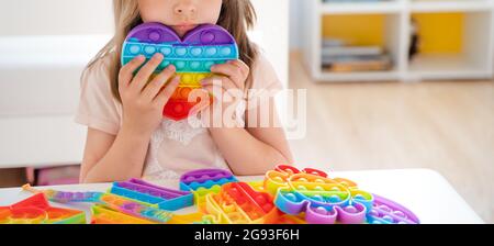 Kleines Mädchen, Kind, Kind spielt mit bunten Pop es Kinderzimmer, Schlafzimmer.Funny trendy Silikon Antistress bunte sensorische Push-Spielzeug popit.Flapping Fi Stockfoto