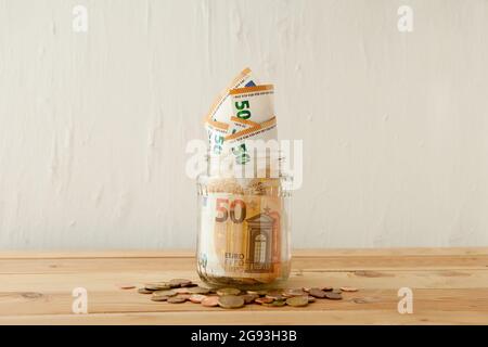 euro-Geldscheine im Glasgefäß am Holztisch mit Euro-Münzen oder Cent. Geschäftskonzept. Geldeinsparungen im Glastopf zu Hause. Stockfoto