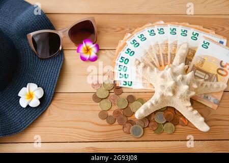 Accessoires für den Sommerurlaub in Europa, auf einem hölzernen Hintergrund - Eruro Geld, Seestar, Sonnenbrille und Hut mit Blumen Stockfoto