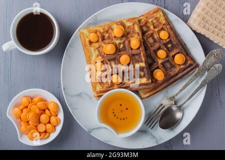 Hausgemachte Waffeln mit orangen Süßigkeiten und Honig auf einem Teller auf einem grauen Tisch Stockfoto