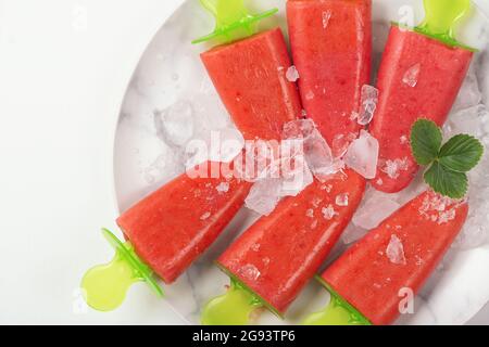 Hausgemachte Erdbeerpopsicles und Eis auf einem Teller auf einem weißen Tisch. Gesundes sommerliches Food-Konzept mit Kopierraum. Stockfoto