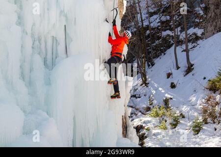 Luftaufnahme eines gefrorenen Wasserfalls und Felsen, bei dem Kletterer seine eisbedeckte Oberfläche mit Eispickeln und Steigeisen aufsteigen Stockfoto