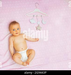 Niedliches Babymädchen und mobile Spielzeuge auf rosa Decke Stockfoto